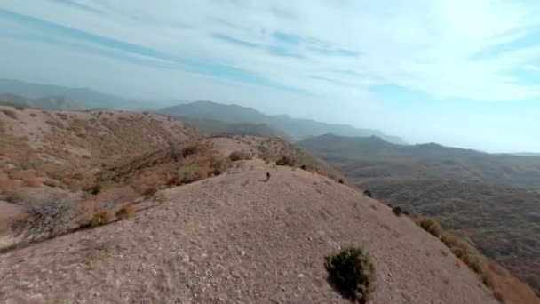 Två professionella idrottare cyklister rida snabba berg mtb e-cyklar längs åsen spår tomma kullar krön i höglandet under blå molnigt himmel drönare första punkten fpv sport följa filmisk antenn vy. — Stockvideo