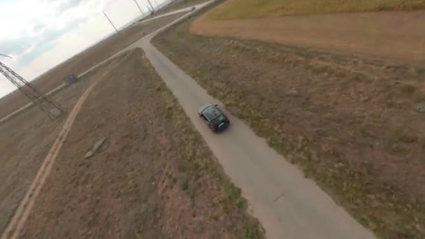 Voiture noire conduit rapidement le long de la route asphale vide passé l'exploitation des moulins à vent autour du champ sous le ciel avec des nuages duveteux fpv freestyle sport drone premier point vue aérienne cinématique — Video