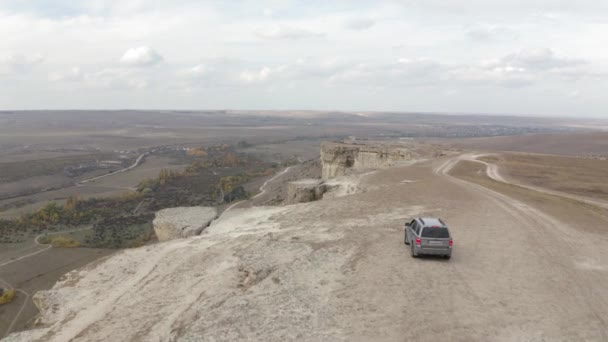 Volare sopra bella formazione scogliera White Rock con auto suv in movimento fermato vicino abisso vista aerea valle naturale. Incredibile paesaggio alpino con cielo nuvoloso infinito e montagne geologiche — Video Stock