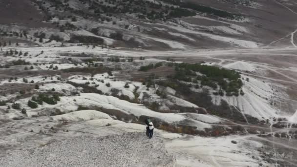 丘陵地帯に囲まれた白い岩の上には、空中のパノラマビューの活発なハイカーカップルが抱きついています。撮影成功した男と女を回転ピーク時の山の愛を感じることは自然の風景を熟考 — ストック動画