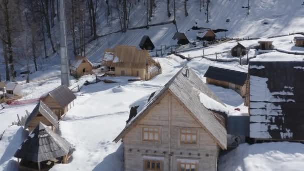 Flying backward over natural landscape winter countryside wooden roof village hut snowy mountains ski resort with cableway. Aerial view ropeway at canyon extreme active lifestyle surrounded woodland — Stock Video