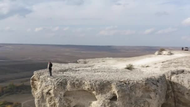 Movimento de velocidade aérea em torno de ver pessoas ativas casal abraçando em cima de White Cliff cercado por terreno montanhoso. Homem e mulher sentindo amor no pico da montanha contemplam a paisagem da natureza — Vídeo de Stock