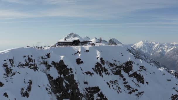 Estación de esquí de montaña con cresta nevada de Aibga y telesilla. Centro turístico nevado en la cima de la montaña. Hermoso acantilado nevado en invierno día soleado. Vista aérea 4k — Vídeo de stock