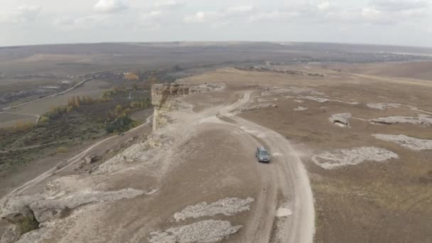 空飛ぶドローンから山の高原の景色を旅するスーパーカー。一方、山の地形で極端な旅行中に未舗装のルート上でオフロード車の運転。空中後方ビュー4k — ストック動画