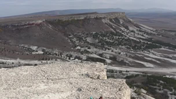 4K aérea atirando para cima textura rochosa. Vista incrível de acima do casal de amor turístico em pé no deck de observação no pico da montanha rocha branca — Vídeo de Stock