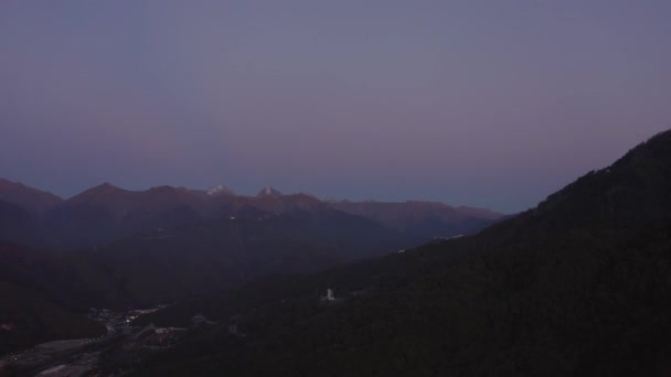 Avondverlichting in de schemering tussen de donkere bergen van drone boven. Moderne avondstad in schemering bergdal luchtfoto 4k — Stockvideo