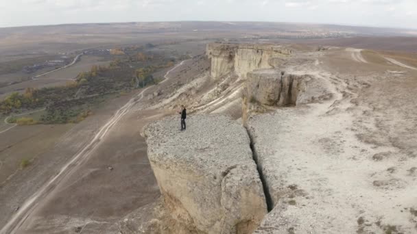 Homem vista aérea em pé no deck de observação com incrível paisagem de montanha. Drone voando para longe de pessoa solitária com um smartphone na mão na borda do penhasco branco no planalto da montanha — Vídeo de Stock