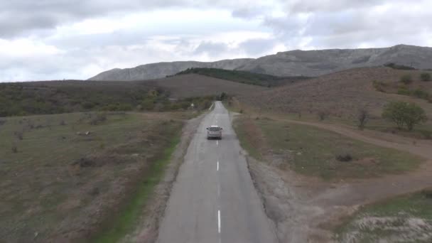 Paysage aérien SUV voiture conduite sur route asphaltée droite sur les collines et le fond de la montagne. Vue sur drone véhicule hors route voyageant sur un paysage sauvage — Video