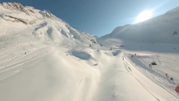 Drone volando cerca de telesilla sobre la montaña nevada en el soleado día de invierno. Pista nevada en la estación de esquí. Manera de cable para el transporte turístico en descenso nevado. Disparo aéreo del avión no tripulado deportivo fpv — Vídeo de stock