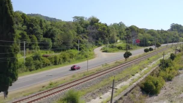 Aerial tracking shot red car riding on speed highway Abkhazia near railroad on coast Black sea road — Stock Video