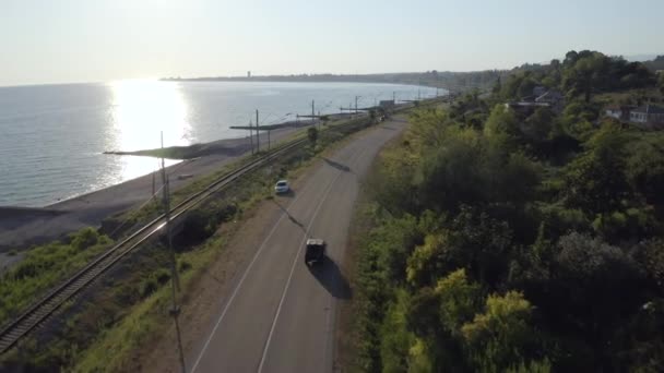 Tiro aéreo voando sobre paisagem marinha da natureza com automóvel SUV dirigindo na estrada de asfalto ao pôr do sol — Vídeo de Stock