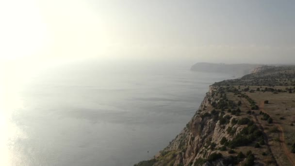 Tiro superior aéreo voando sobre o brilho incrível do sol do mar e montanhas altas do penhasco na vista do pôr do sol do verão — Vídeo de Stock