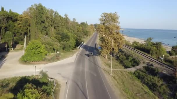 Black suv car drives along grey asphalt coastal road between green forest — Stock Video