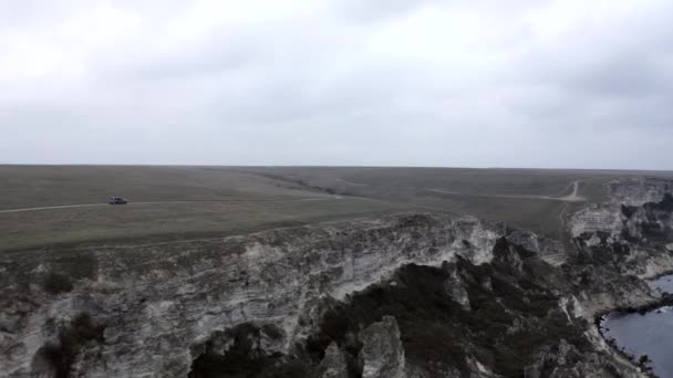 Стрілянина з безпілотника позашляховик їде по дорозі на вершині високої скелі біля природного моря гори — стокове відео