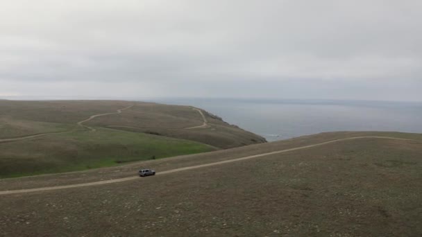 Flygfoto runt visa skott hög hastighet SUV bil kör på toppen av bergsvägen naturlig himmel havsutsikt — Stockvideo