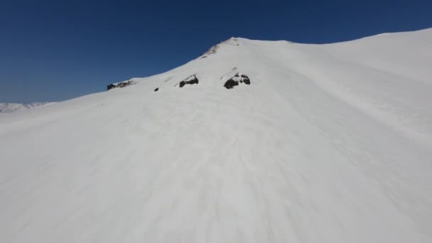 Klettern in der Nähe einer weichen, glatten Schneedecke auf einem hohen Berggipfel unter blauem Himmel Luftaufnahme — Stockvideo