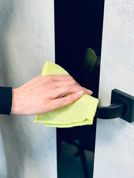 The girl cleans the handle of the front door with a yellow napkin with an antiseptic, disinfectant. Close-up. Grey background.