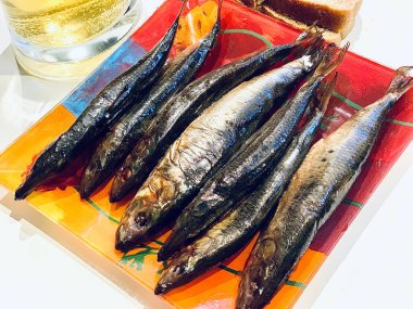 Beyaz arka planda renkli bir tabakta altın renginde küçük tuzlu balıklar. Bira çerezi. Yakında bir bardak bira var..