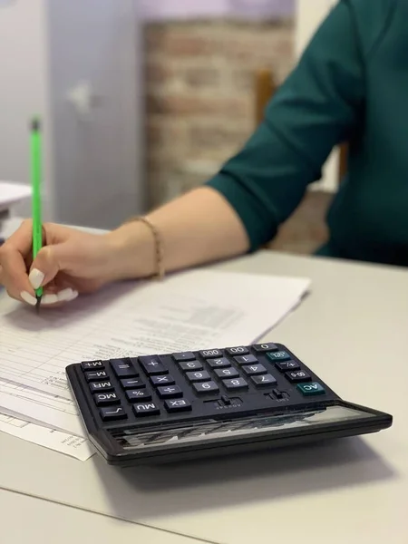A woman in the office writes with a pencil and counts on a calculator.