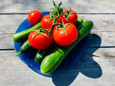 Gri ahşap arka planda bir tabakta kırmızı domates ve salatalık..