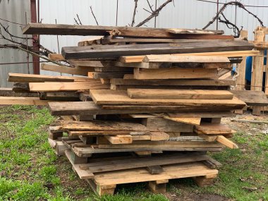 Yerde, yeşil çimlerin üzerinde düzgünce istiflenmiş bir odun yığını ya da kereste yığını yatıyor. Tahtaların kuruması.