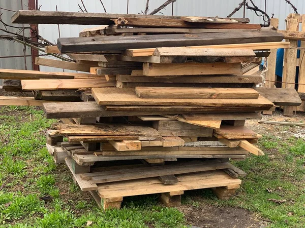 On the ground, in the green grass, lies a neatly stacked pile of planks or lumber. Drying of wooden boards.