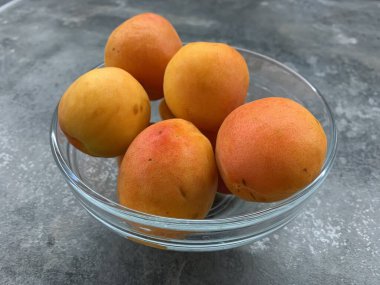 Gri arka planda şeffaf bir tabakta taze kayısılar. Boşluğu kopyala.