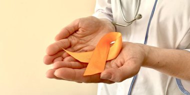 Orange ribbon in the hands of a doctor. Multiple sclerosis, oncology awareness concept. 