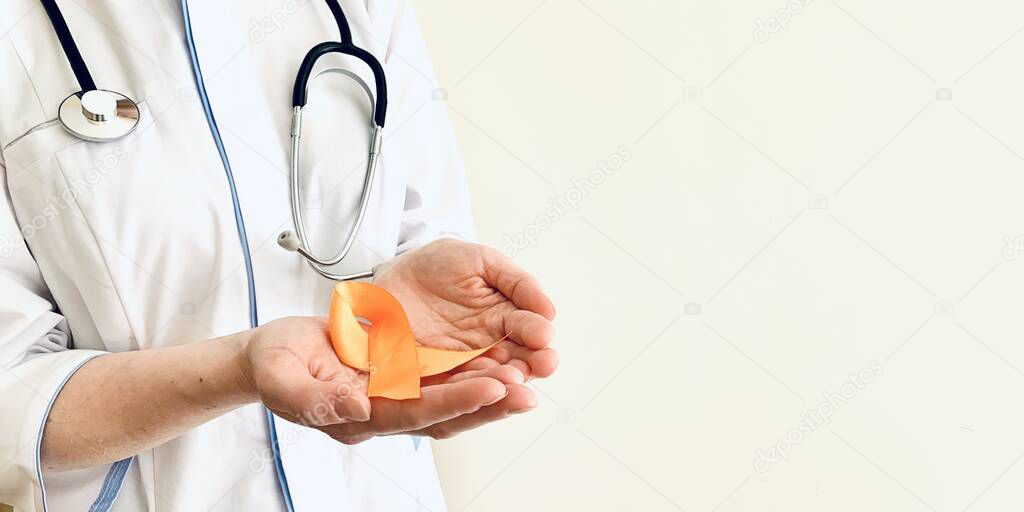 Orange ribbon in the hands of a doctor. Multiple sclerosis, oncology awareness concept. Place for your text.