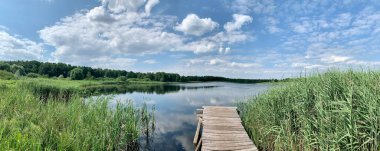 Panoramic view of the lake, blue sky with clouds. Wooden path in the lake. clipart