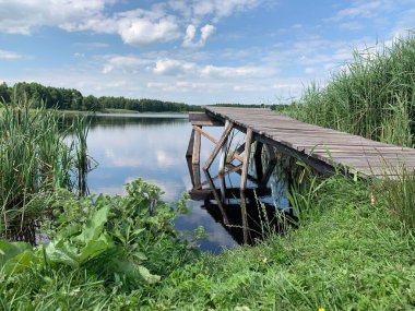 Göl manzarası, bulutlu mavi gökyüzü. Göldeki tahta patika..