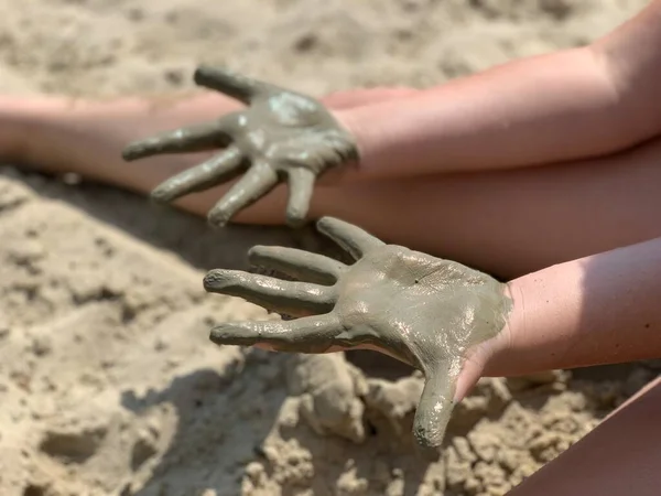 The girl plays with sand and smears her hands. Hands in the beach wet sand.