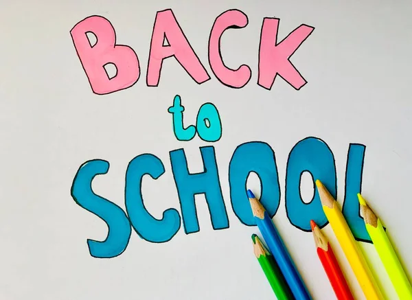 Back to school. Inscription in colored letters on a white background. Nearby are colored pencils.