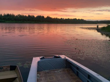 Gün batımında nehir manzarası. Kıyıya yakın tekneler var..