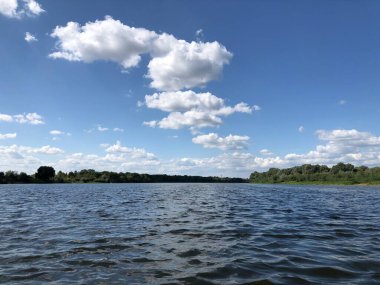 Nehir kıyısı, beyaz bulutlu mavi gökyüzünün arka planına karşı..