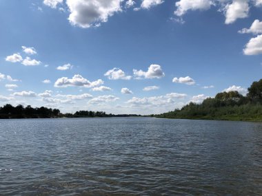 Nehir kıyısı, beyaz bulutlu mavi gökyüzünün arka planına karşı..
