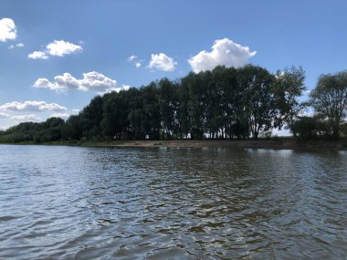 Nehir kıyısı, beyaz bulutlu mavi gökyüzünün arka planına karşı..
