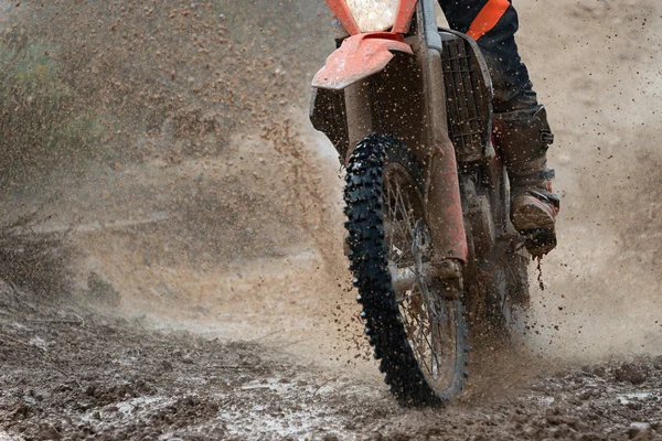 Motocross driver splashing mud on wet and muddy terrain