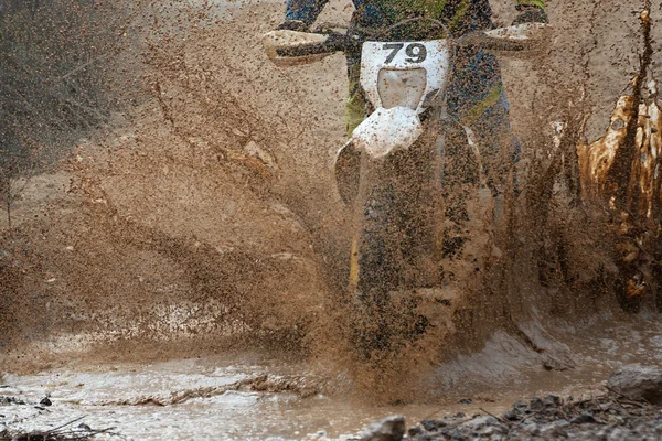 Motocross driver splashing mud on wet and muddy terrain