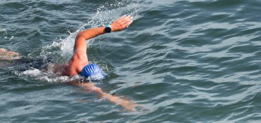 Yüzen adam mavi denizde sürünüyor, triatlon için yarışıyor.
