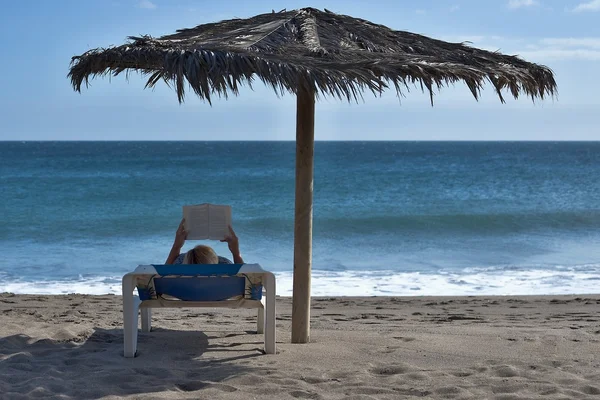 Mujer leyendo libro sobre chaise longue en la playa — Foto de Stock
