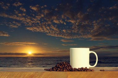 Coffee cup on wood table at sunset or sunrise ocean
