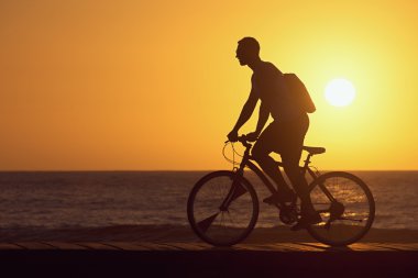 Genç adam bisikletçi Sunset'teki silüeti