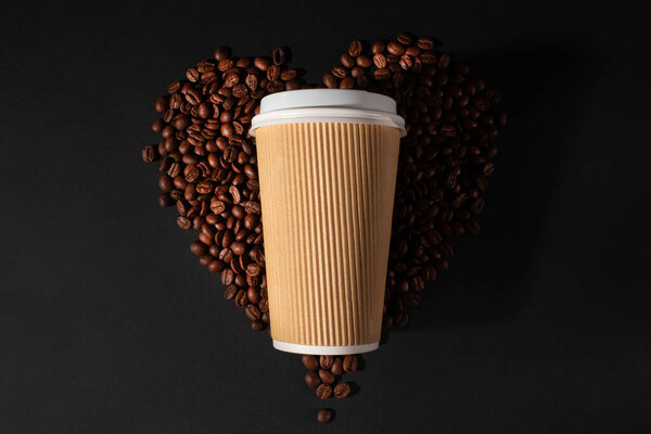 Paper cup of coffee with coffee beans on black background. Top view. Coffee lovers.