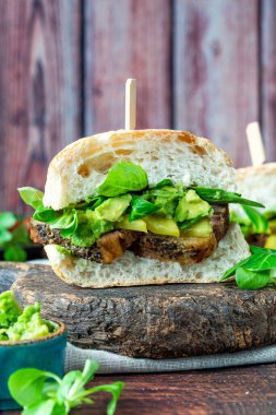 Salatalık turşulu biftekli sandviç, ezilmiş avokado ve yeşil yaprak salatası.