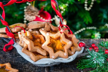 Arka planda Noel ağacı olan ahşap masa üzerindeki vitraylı cam bisküvi yığını..