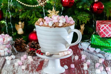 Krem şantili sıcak çikolata ve arka plandaki ağacın altında noel hediyeli şekerlemeler.