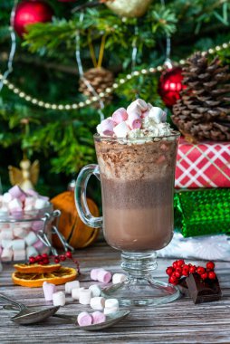 Krem şantili sıcak çikolata ve arka plandaki ağacın altında noel hediyeli şekerlemeler.