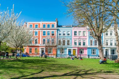 Londra, İngiltere - 29 Mart 2021: İnsanlar Chalcot Meydanı Bahçeleri 'nde renkli İtalyan teraslı evlerle çevrili güneşin tadını çıkarıyorlar. Primrose Hill 'in Büyük Londra Bölgesi filmlerde ve televizyonlarda sıklıkla kullanılır.