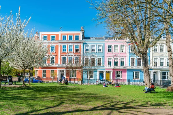 Londra, İngiltere - 29 Mart 2021: İnsanlar Chalcot Meydanı Bahçeleri 'nde renkli İtalyan teraslı evlerle çevrili güneşin tadını çıkarıyorlar. Primrose Hill 'in Büyük Londra Bölgesi filmlerde ve televizyonlarda sıklıkla kullanılır.